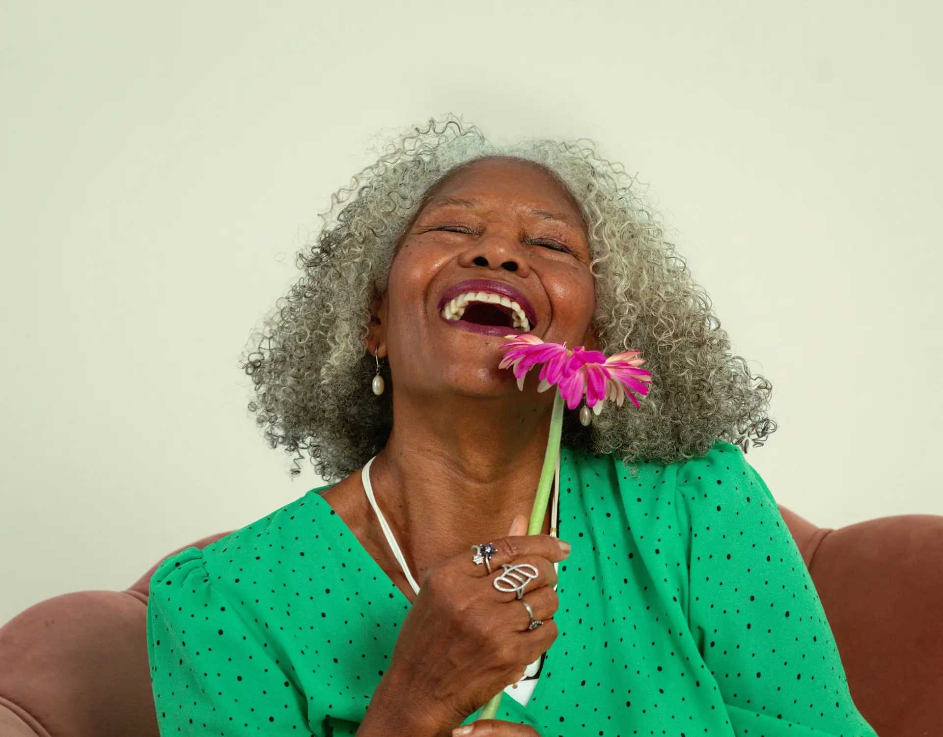 Portrait of a joyful senior woman laughing with a pink flower in hand.